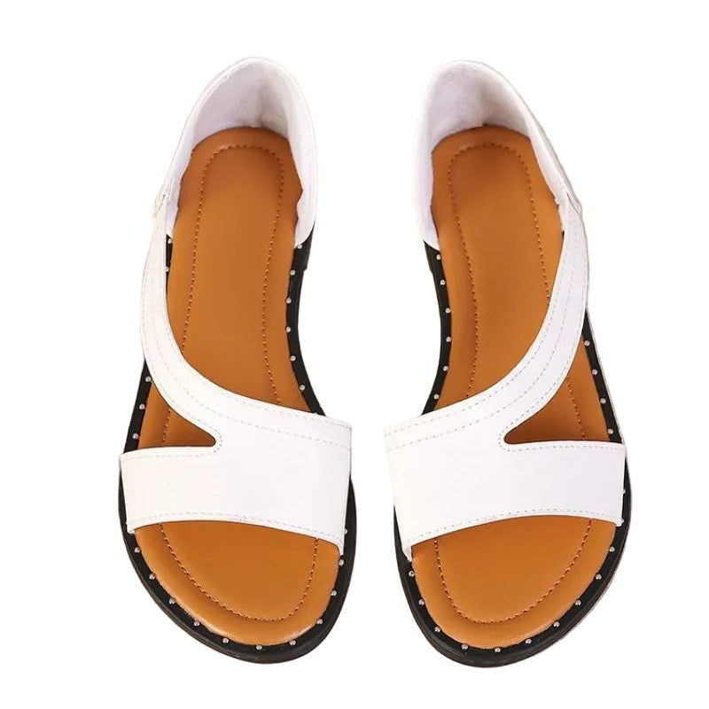 Pair of white sandals with brown soles on a beige surface