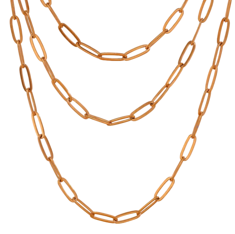 A gold-toned paperclip chain necklace with three layered strands, displayed against a soft, light pink background.