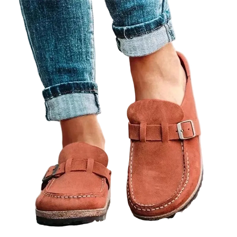 Brown loafers with buckles worn with rolled-up jeans on a light background