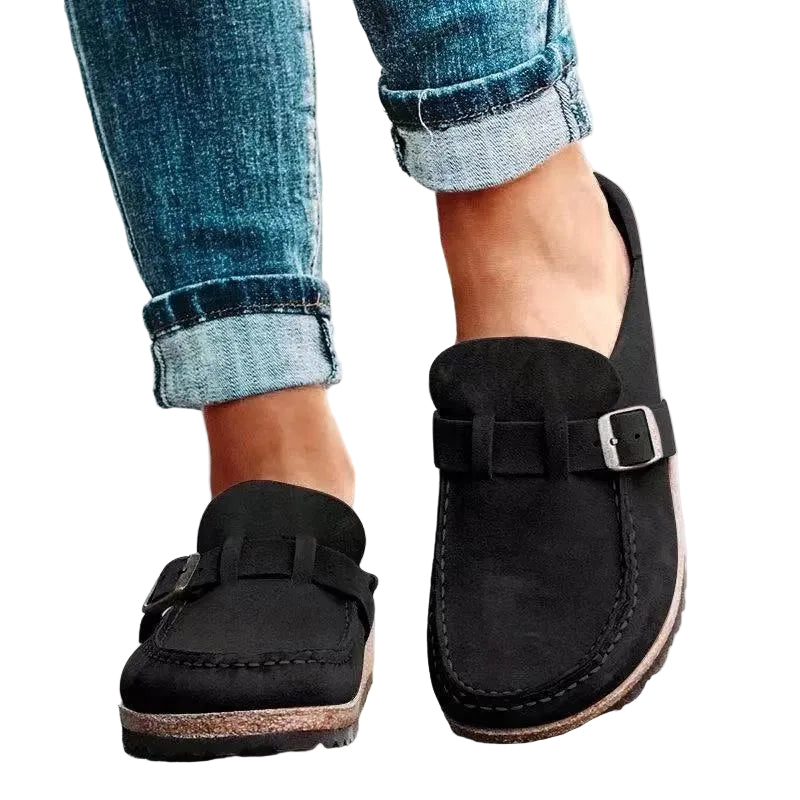 Black loafers with buckles worn with rolled-up jeans on a light background
